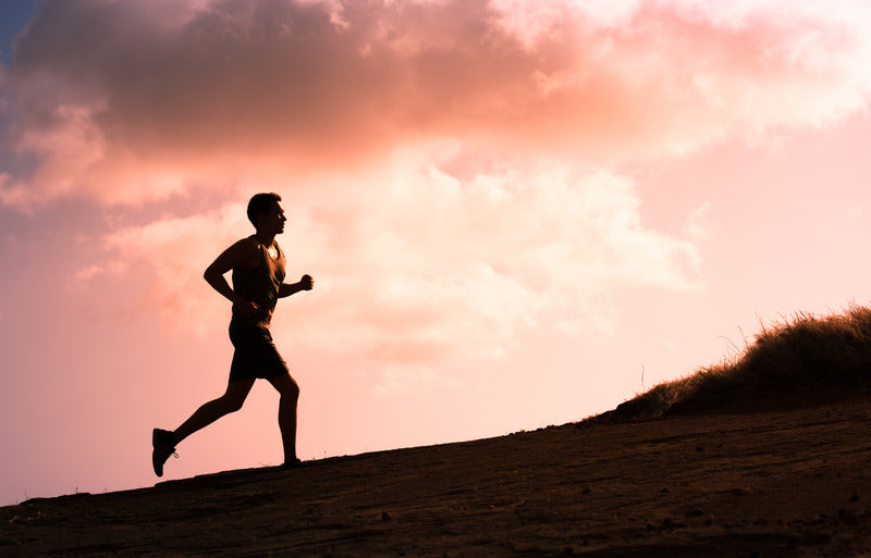 A man running along a scenic road with mountains and a lake in the background.