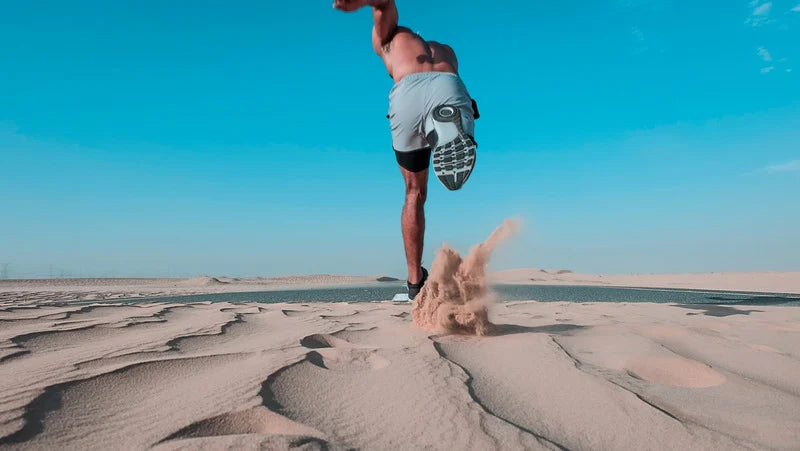 A man running on a sandy desert road, kicking up sand.