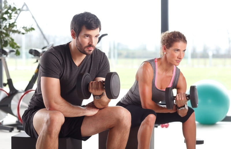 A shirtless man lifting a dumbbell with a brick wall background.